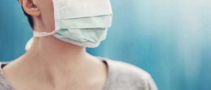 young woman in medical face protection mask indoors on blue background. Sick person