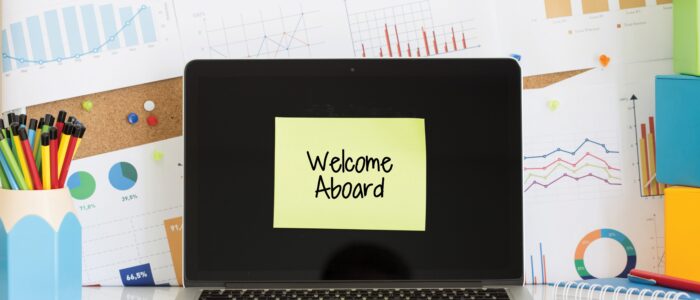 WELCOME ABOARD sticky note pasted on the laptop screen